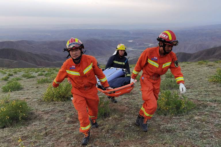 homens vestidos de laranja carregam equipamento em uma montanha