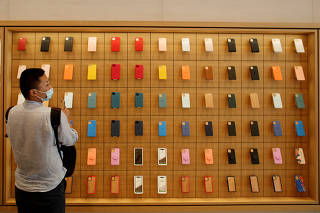 FILE PHOTO: A man stands in front of a wall of iPhones cases in Beijing