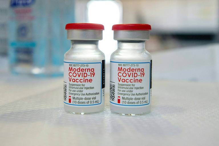 Frascos da vacina da Moderna; são dois, transparentes, com tampa metálica e vermelha, o rótulo também tem as letras em vermelho