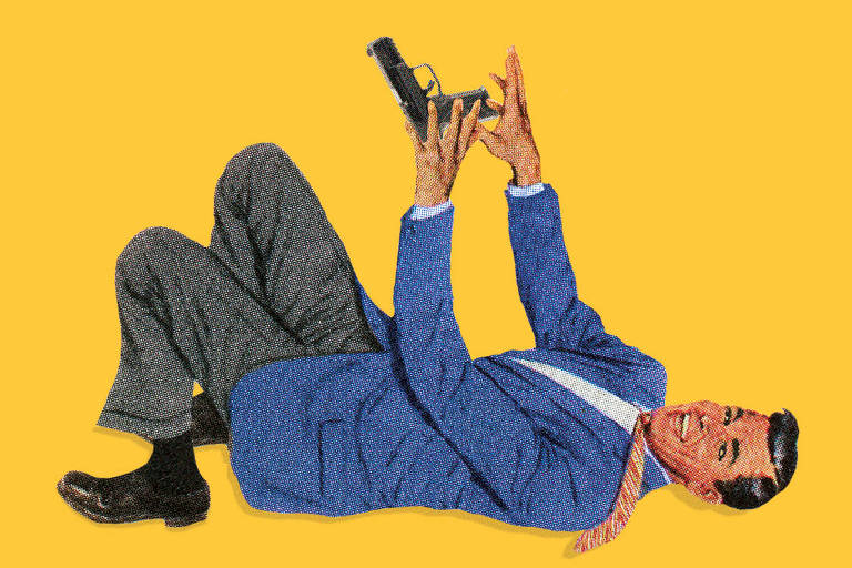 Homem branco usa roupa social e está deitado no chão enquanto segura arma de fogo sorrindo