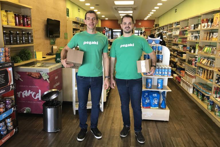 Os sócios da Pegaki João Cristofolini (CEO), à esquerda, e Daniel Frantz (COO), à direita, fundadores startup criada em SC e que foi adquirida neste ano por grupo de logística; eles estão em um dos 2.000 pontos de coleta e retirada de mercadorias (padarias, mercado, lojas de conveniência, etc.) para quem vende e compra em ecommerces
