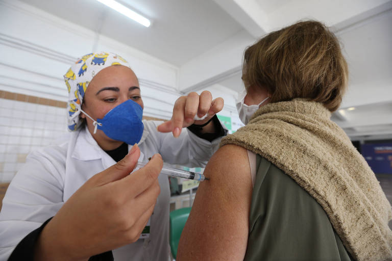 Mulher aparece aplicando vacina no braço de outra mulher