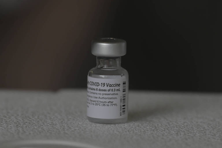 Frasco de vacina da  Pfizer contra a Covid-19; vidro transparente, com rótulo branco e tampa prateada