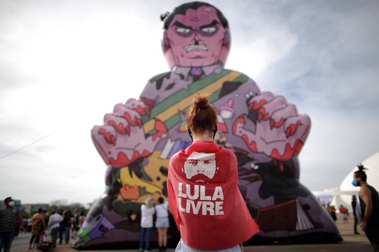 Manifestante, enrolada em bandeira de apoio a Lula, tira foto de boneco inflável que representa o presidente Jair Bolsonaro durante protesto em Brasília