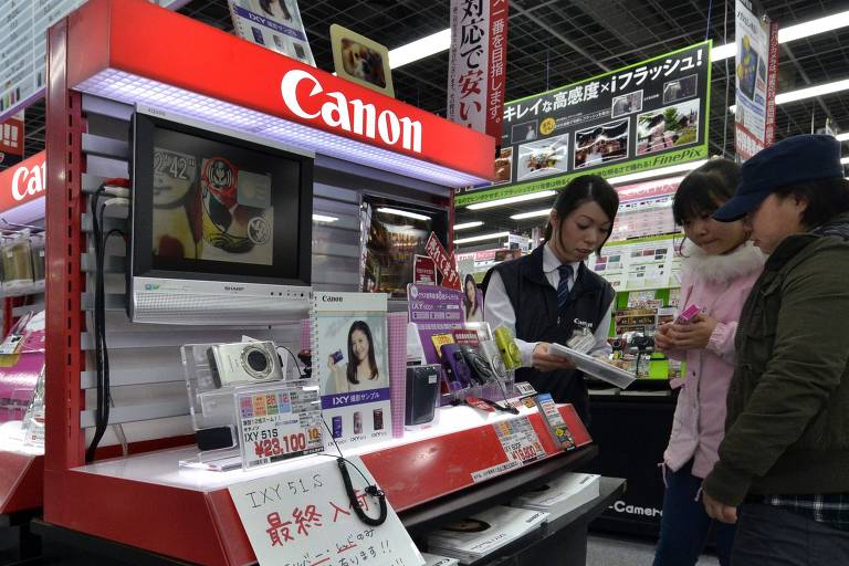 Casal de japonesas e vendedora observam produtos da marca de câmeras Canon 