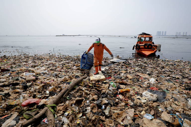 Pessoa anda por meio de lixo plástico qna costa da Indonésia 
