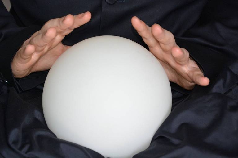 Bola de cristal sendo manuseada por mãos brancas, diante de um fundo preto