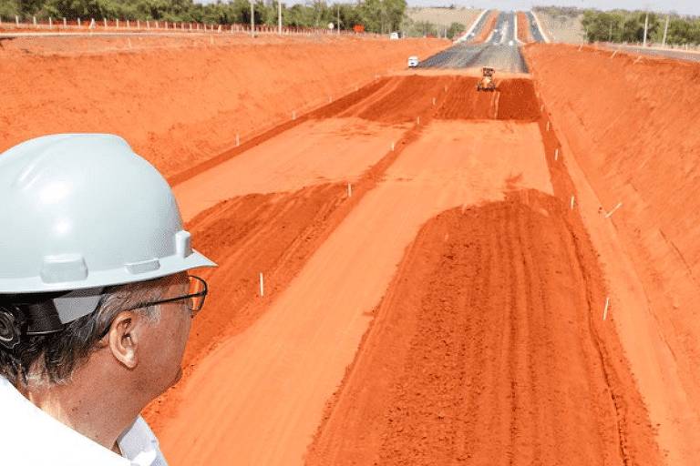 Imagem muito semelhanda à da foto acima, mas, nesta, no canto esquerdo inferior está Geraldo Alckmin, de camisa e capacete brancos, de perfil, olhando para o horizonte da estrada