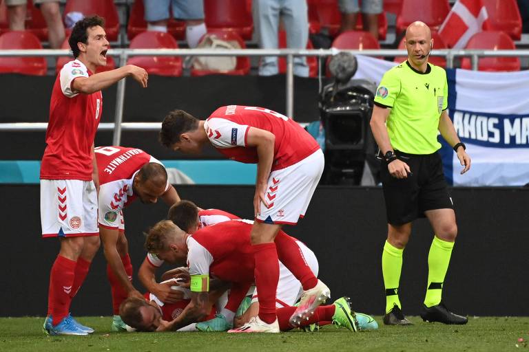 Jogadores da Dinamarca tentam ajudar Eriksen após o jogador cair no gramado
