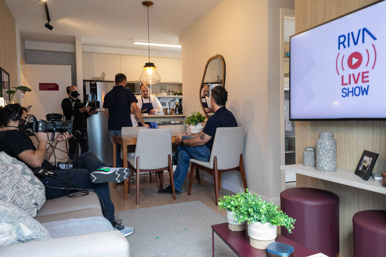 Sala de apartamento com pessoas sentadas de costas e câmeras filmando