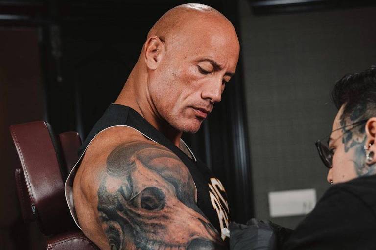 Homem branco e careca mostrando tatuagem em bíceps direito
