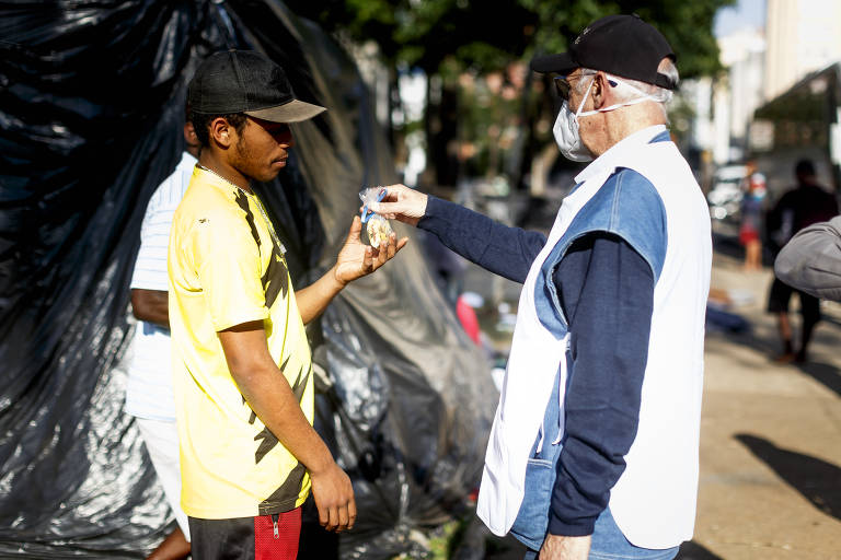 O padre Júlio Lancellotti, da Pastoral do Povo de Rua, dá um saquinho com chocolates para um morador de rua, na praça Princesa Isabel (região central de São Paulo). Ele também doou água e marmitas para as pessoas da região. O padre participou da doação de kits de inverno da Cruz Vermelha São Paulo.