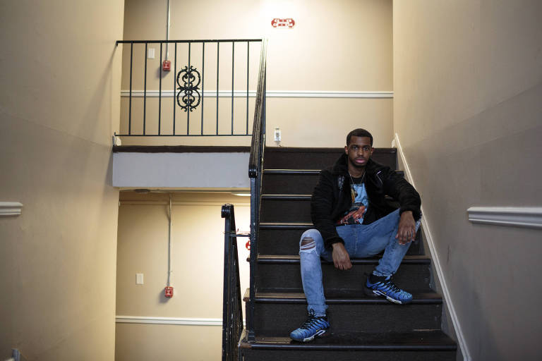 Homem negro posa sentado com as pernas abertas em uma escada