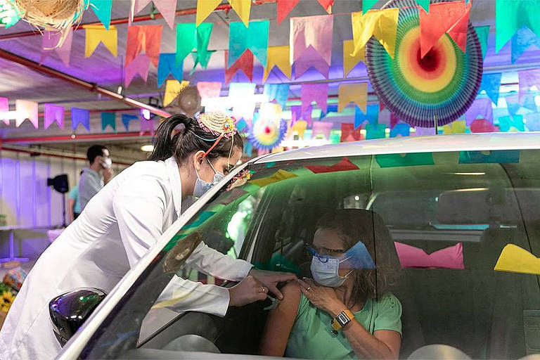 Mulher dentro do carro recebe vacina de funcionário, com enfeites juninos no entorno