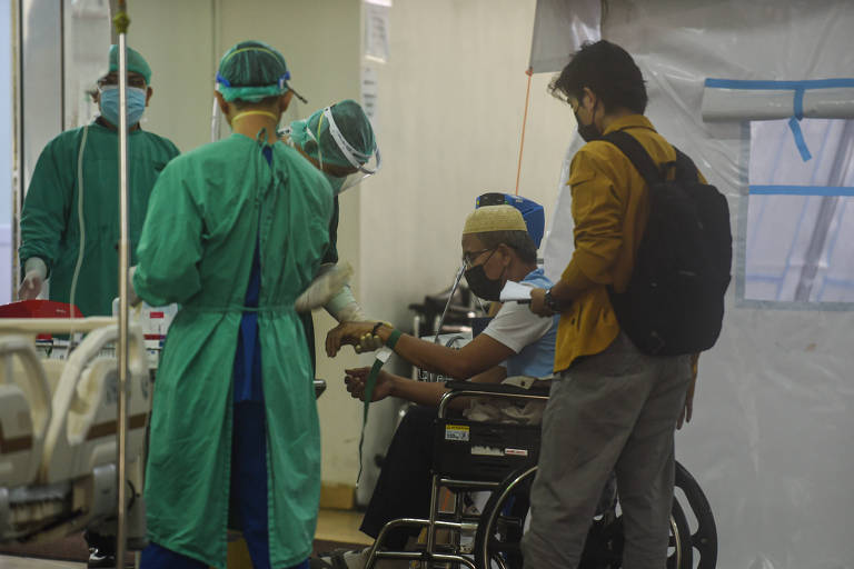 Médicos cuidam de paciente, sentado em cadeira de rodas, com Covid-19, na Indonésia