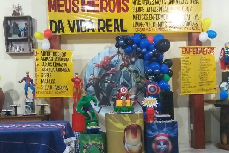 Imagem mostra super-heróis e decoração de aniversário de uma criança, com faixas e cartazes homenageando médicos