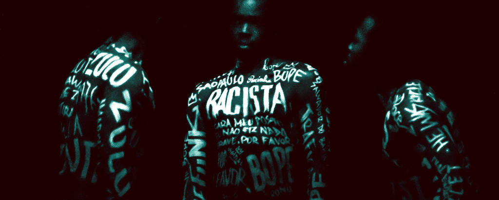 Três homens negros com o torso pintado com palavras brancas que remetem ao racismo