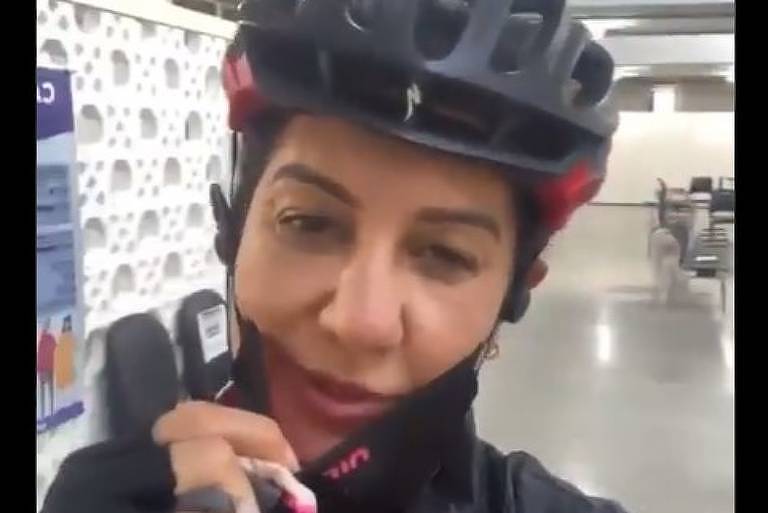 Fernanda Venturini, com capacete e trajes de ciclista, está um local para  receber a primeira dose da vacina contra a Covid, em São Paulo