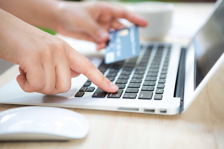 Mão segurando um cartão de crédito e usando computador para comprar online