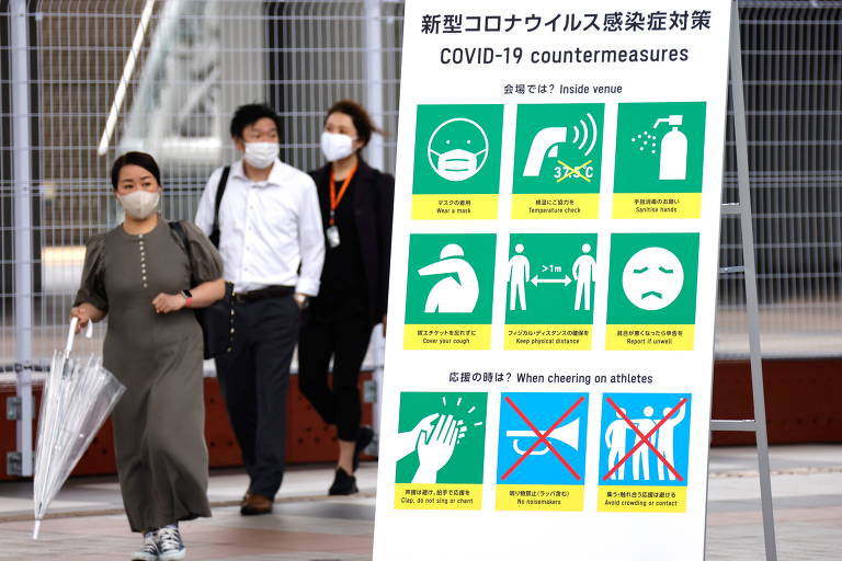 Pessoas deixam o Centro de Mídia dos Jogos de Tóquio. Em primeiro plano, cartaz mostra regras seguidas no prédio para conter disseminação do novo coronavírus
