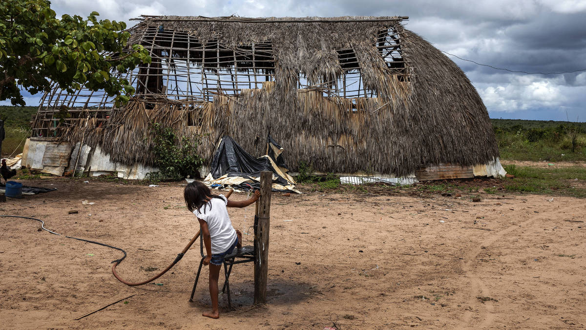 Menina do povo Haliti Paresi lava os pés em uma torneira em frente a uma hati, casa tradicional, na aldeia da Terra Indígena Figueiras, localizada entre os municípios de Barra do Bugres e Tangará da Serra
