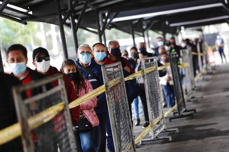 Fila com dezena de pessoas em Bogotá, na Colômbia, de máscara e separadas por faixas e grades, aguardando para tomar vacina contra a Covid-19