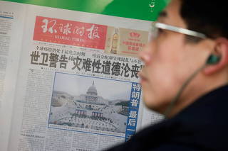 Man stands in front of a copy of the Global Times newspaper placed on a public display window in Beijing