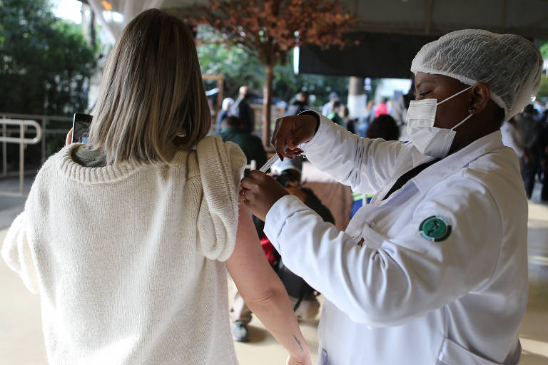 Profissional de saúde negra aplica vacina contra a Covid-19 em mulher branca