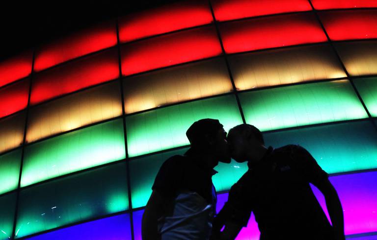 Dois homens se beijam diante de uma parede de luzes nas cores do arco-íris durante o Dia Internacional do Orgulho LGBT, em 2021