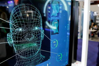 FILE PHOTO: Visitors check their phones behind the screen advertising facial recognition software during Global Mobile Internet Conference (GMIC) at the National Convention in Beijing