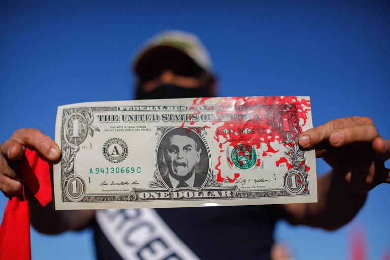 Manifestantes em Brasília segura dólar falso com efígie de Bolsonaro, em alusão à suposta propina de US$ 1 por dose de vacina cobrada por funcionário da Saúde