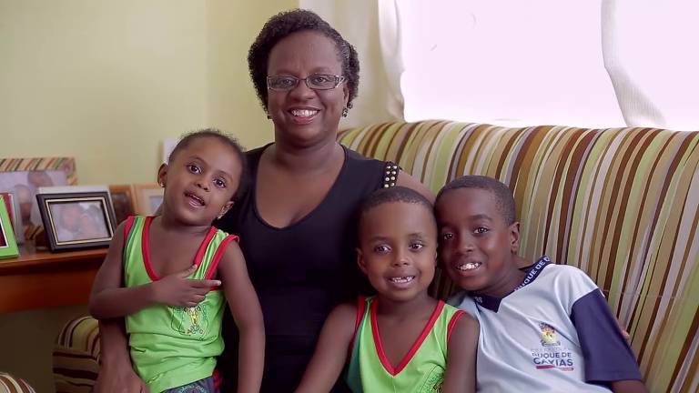 mulher negra sentada em sofá na companhia de três filhos
