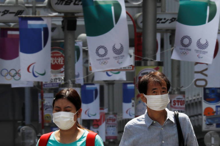 Pedestres, protegidos por máscaras, passam por faixas relativas à Olimpíada de Tóquio