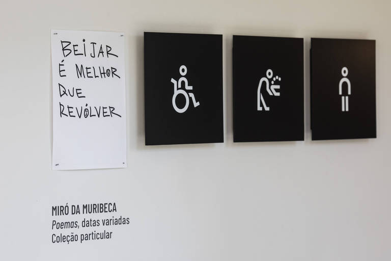 Uma parede com quatro elementos. À esquerda, há um cartaz com a frase 'BEIJAR É MELHOR QUE REVIVER'. À direita, três quadros pretos com símbolos brancos: um símbolo de acessibilidade, uma figura humana em movimento e uma figura humana em pé.