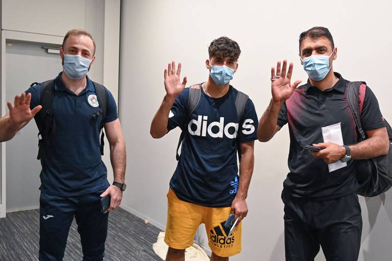 Os atletas Ahmad Alikaj e Abdullah Sediqi e o técnico Alireza Nassrazadany, do time de refugiados, chegam ao aeroporto de Narita, no Japão. Os três acenam a mão
