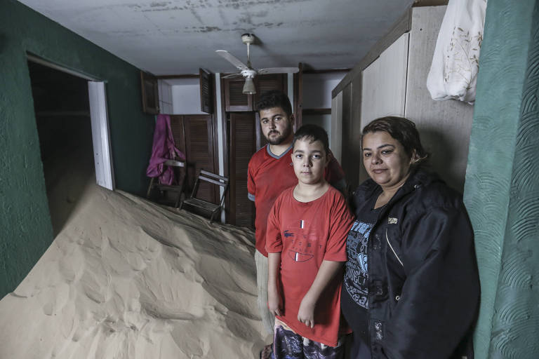 mulher com filhos em sala coberta por montanha de areia da duna
