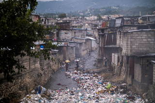 People cross a stream clogged by garbage next to houses in Port-au-Prince