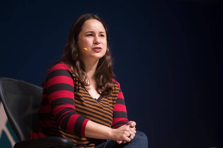 A escritora Ana Martins Marques está sentada com uma camisa listrada discursando durante evento da FLIP 2013