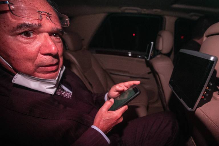 O ministro Paulo Guedes mexe em um celular sentado no banco de trás de um carro