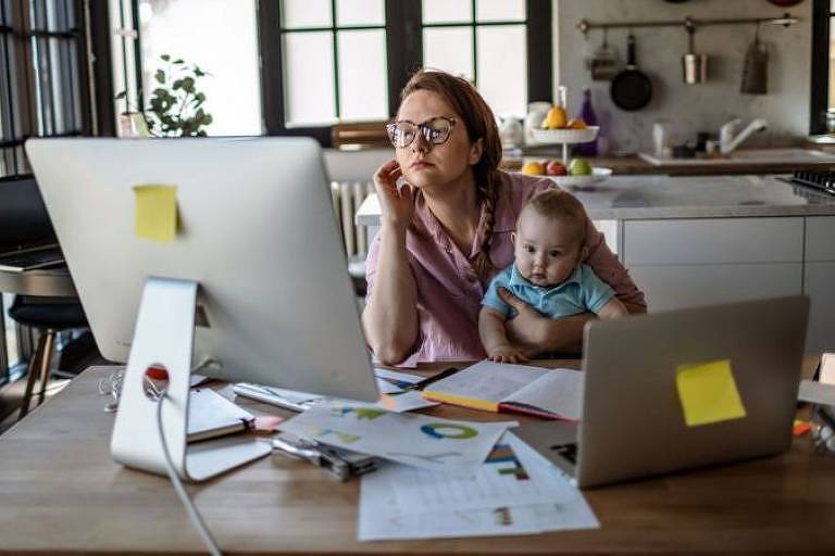 Mulher branca trabalhando no computador com bebê no colo