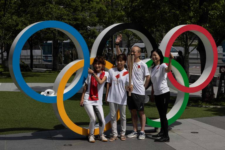 Pessoas posam à frente dos anéis olímpicos, junto com a tocha olímpica