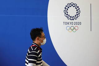 A man wearing a face mask walks past Tokyo 2020 Olympic Games signage at the Main Press Center in Tokyo