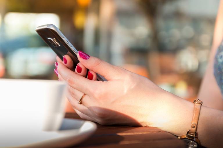 mãos femininas seguram um celular sobre uma mesa