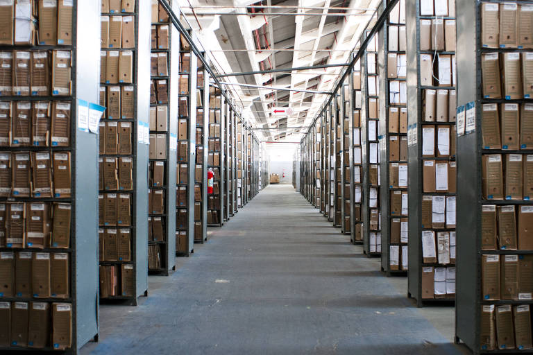 Um corredor com vários estantes dos dois lados, carregadas com caixas de arquivo