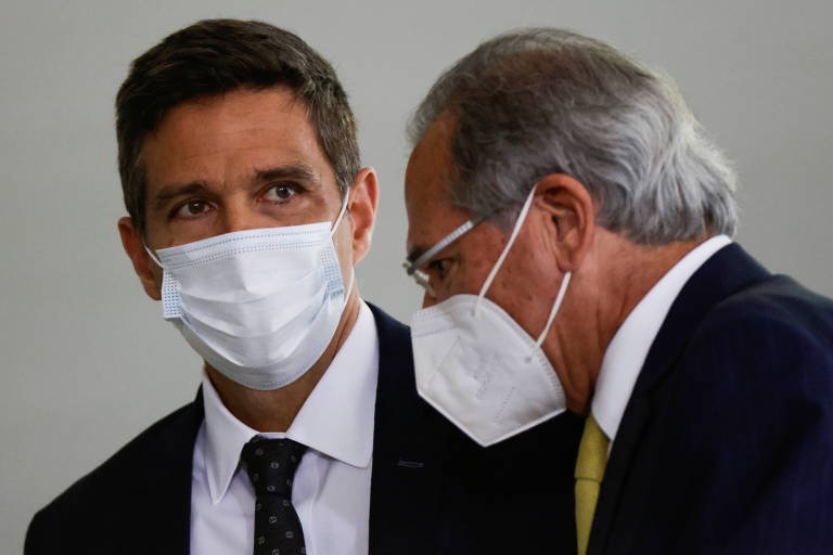 O presidente do BC, Roberto Campos Neto (esq.), com o ministro Paulo Guedes , ambos de máscara e terno, de pé
