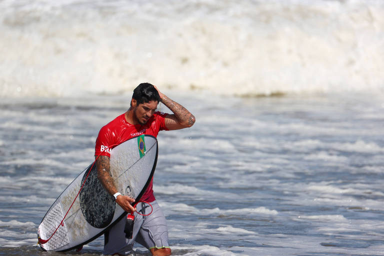 Surfista sai de cabeça baixa do mar, segurando sua prancha