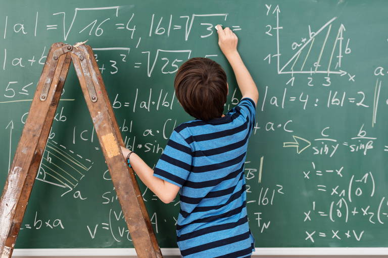 Lousa verde com números, cálculos e gráficos desenhados em giz branco e um menino de costas usando uma camiseta listrada de azul e preto escrevendo, com a mão apoiada em uma escada de madeira