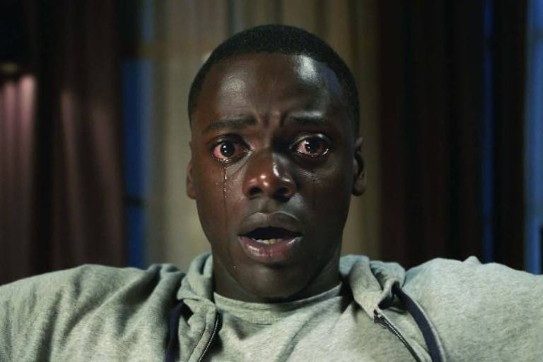 Cena do filme "Corra!" mostra personagem negro com olhos arregalados e boca aberta, com expressão de espanto, encarando o espectador.