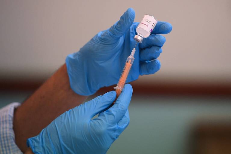 Farmacêutico, de luvas azuis, segura uma seringa, enquanto prepara dose de vacina contra a Covid-19 em centro de vacinação temporário em Birmingham, na Inglaterra