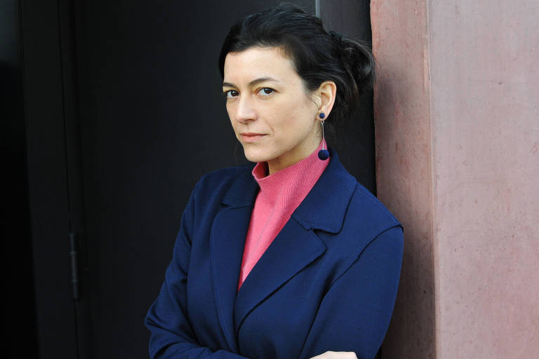 mulher branca de cabelos escuros e longos usando calça jean e casaco preto